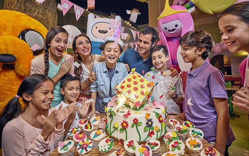 Birthday party celebration at IMG Worlds of Adventure with kids, parents, a themed cake, and cartoon character